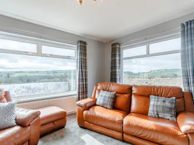 a living room with a leather couch and two windows at 3 Bed in Auldgirth 77430 in Auldgirth