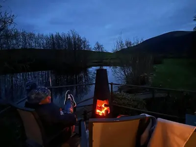 a man sitting in a chair next to a fire at The Lily Pod in New Abbey