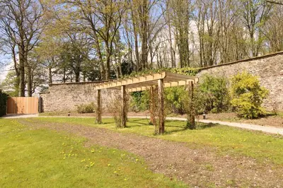 a wooden arbor in a field next to a brick wall at Shepherds Retreat Hutton John in a walled garden in a rural setting only 10 minutes for Lake Ullswater in Penruddock
