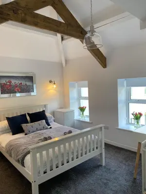 a bedroom with a white bed and two windows at The Cottage, Bridge House in Laxey