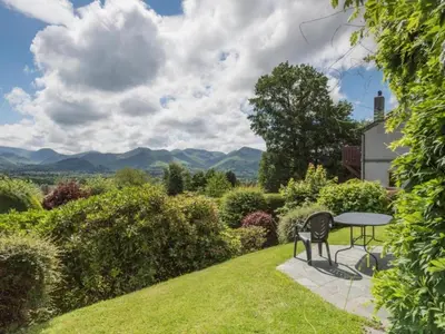 a table and chairs in a garden with mountains in the background at 3 Bed in Applethwaite SZ328 in Applethwaite