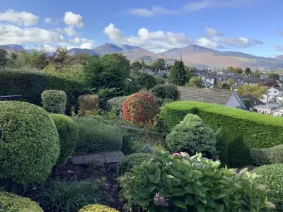 a garden with bushes and trees with mountains in the background at 1 Bed in Keswick oc-sz437 in Keswick