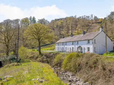 a white house on a hill with a river in front at 3 Bed in Borrowdale SZ234 in Rosthwaite