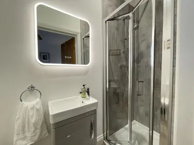 a bathroom with a shower and a sink and a mirror at Langrigg Cottage HOT TUB HIRE AVAILABLE in Portinscale