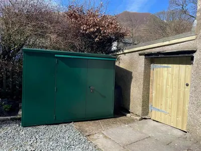 a green garage with a wooden door next to a house at 2 Bed in Keswick oc-90064 in Threlkeld