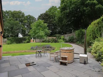 a patio with a table and a barrel in a garden at The Gardener's Retreat in Penrith