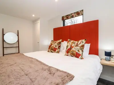 a bedroom with a large white bed with a red headboard at The Gardener's Retreat in Penrith