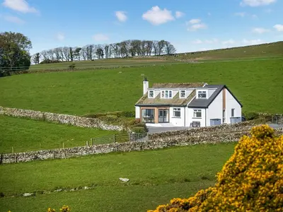 a white house in a field with a stone wall at High Auchenlarie Cottage in Carsluith