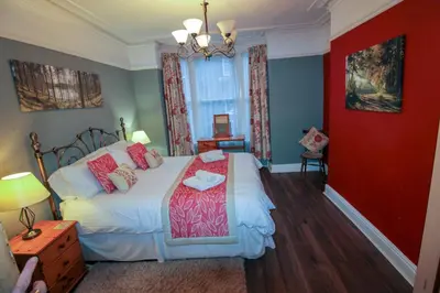a bedroom with a bed and a red wall at Carlton Cottage all ground floor, centrally located in Keswick in Keswick