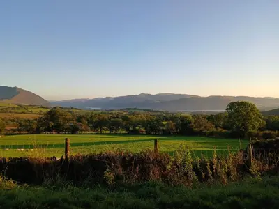 a field with a fence and mountains in the background at Emilys Nook Ireby, budget accommodation with fell views in Ireby
