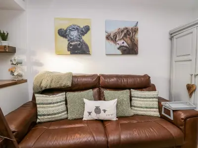 a brown leather couch sitting in a living room with paintings at High Wreah Bolt Hole in Whitehaven