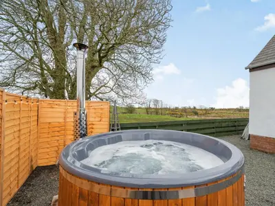 a hot tub in a wooden fence with a tree at 3 Bed in Mochrum 87541 in Mochrum