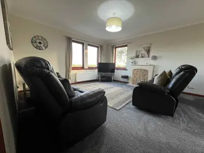 a living room with two chairs and a clock on the wall at 3 Bed in Mochrum 87541 in Mochrum