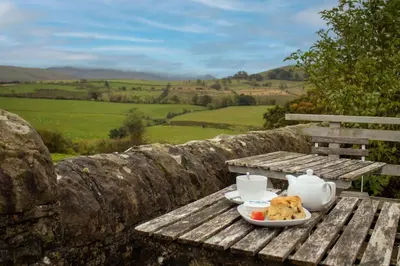 a table with a plate of food and tea on it at Shepherds Hut at Maes Uldale stunning fell views and next door to popular cafe for sweet treats in Uldale