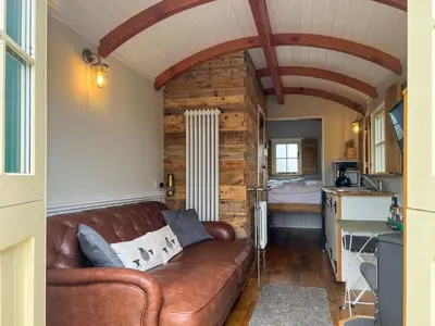 a brown leather couch in a room with a kitchen at Shepherds Hut at Maes Uldale stunning fell views and next door to popular cafe for sweet treats in Uldale