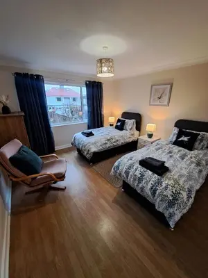 a bedroom with two beds and a chair and a window at 17 The Park in Onchan