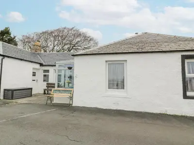 a white house with a bench in the driveway at Rosalin Cottage in Irvine