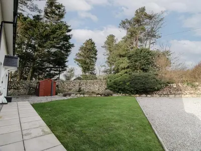 a garden with a stone wall and a red door at Merse End in Dalbeattie