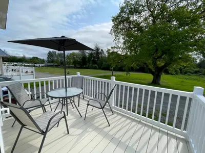 a porch with chairs and a table with an umbrella at Beautiful Cosy Holiday Home in Gorgeous Location - Pass the Keys in Beattock
