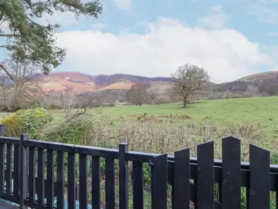 a fence with a field and hills in the background at Hayeswater Lodge in Keswick