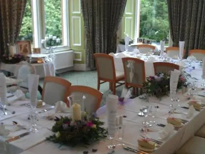a dining room with white tables and chairs with flowers at Kirkconnel Hall Hotel in Lockerbie