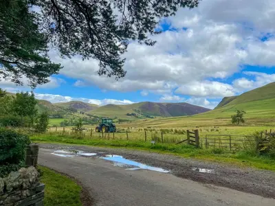a dirt road in a field with mountains in the background at Fell View Bassenthwaite, rural location on a working farm in the fells in Bassenthwaite