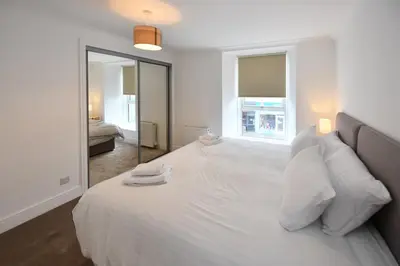 a bedroom with a white bed with pillows and a mirror at Troon Portland Apt A in Troon