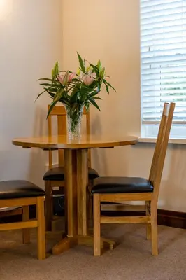 a vase of flowers on a wooden table with chairs at Acorn Apartment 2 (upper) in Keswick