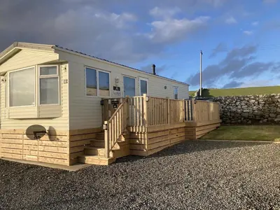 a tiny house with a wooden deck and a stone wall at Beautifully Presented 2 Bedroom Static Caravan in Monreith
