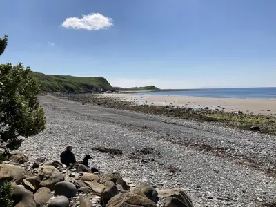 a man sitting on the rocks on a beach at Beautifully Presented 2 Bedroom Static Caravan in Monreith