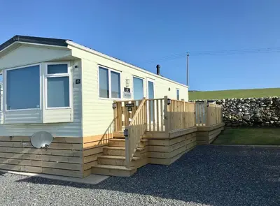 a tiny house with a wooden deck and a stone wall at Beautifully Presented 2 Bedroom Static Caravan in Monreith
