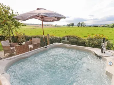 a hot tub with an umbrella and chairs at Plot 32 in Carlisle