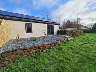 a house with a stone retaining wall next to a yard at The Nest by Blake view holidays, a peaceful boutique retreat, 3 miles from Ennerdale- small twin or king bed available in Rowrah