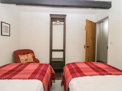 a bedroom with two beds and a chair and a ladder at Church How Cottage in Seascale