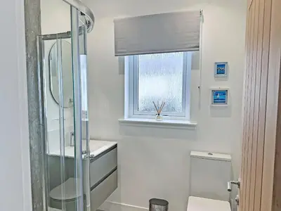 a bathroom with a shower and a toilet and a window at Flag Cottage in Carsethorn