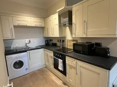 a kitchen with white cabinets and a washer and dryer at Thurnams House, Ground Floor Apt in Carlisle