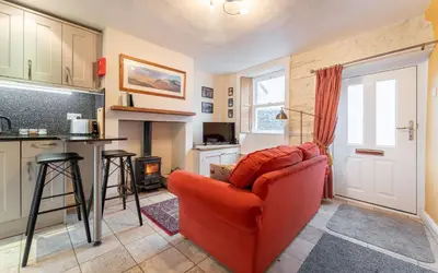 a living room with a red chair and a kitchen at Beagle Cottage in Keswick