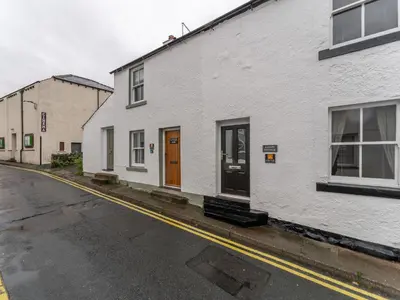 a white building with a brown door on a street at Darwin Cottage in Keswick