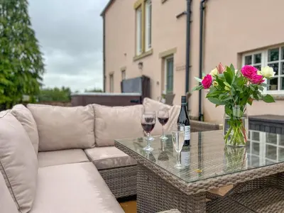 a couch and a table with wine glasses and flowers at High House Cottage, Southwaite in a rural setting with garden, BBQ & hot tub in Southwaite