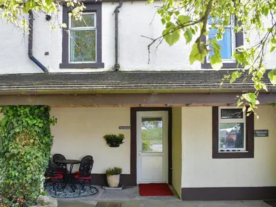 a house with a white door and two chairs at The Stables in Beckfoot