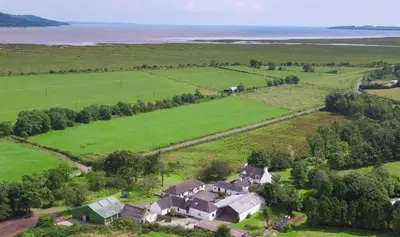 an aerial view of a house in a field and the ocean at Courtyard Cottages Granary Cottage in Wigtown