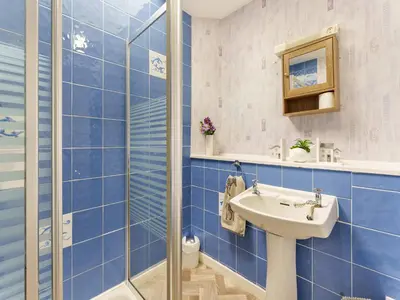 a blue tiled bathroom with a sink and a shower at Carraig Dhubh Cottage - Uk47123 in Whiting Bay