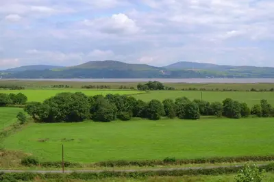 a green field with trees and mountains in the background at Courtyard Cottages Rose Cottage in Wigtown