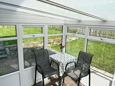 a screened in porch with a table and chairs at Barnbackle Cottage in Shawhead