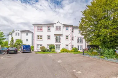 a large white house with cars parked in a parking lot at The Hytte, 19 Greta Grove House in Keswick