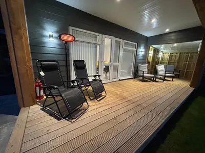 a large wooden deck with chairs and a table at Castle Glen Lodge in Dumfries