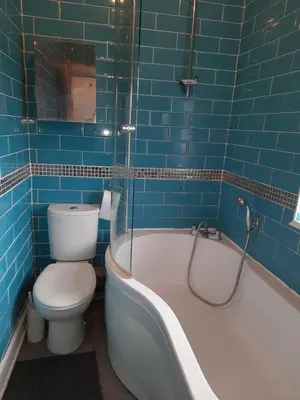 a blue tiled bathroom with a toilet and a bath tub at Smriti's in Dumfries
