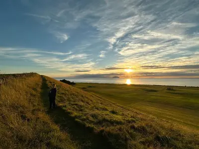 a man walking down a hill in a field with the sunset at Peel House Bed and Breakfast in Girvan