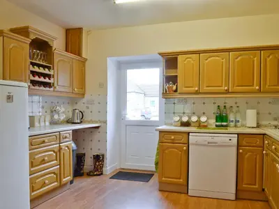 a kitchen with wooden cabinets and a white dishwasher at Park Cottage in Gatehouse of Fleet