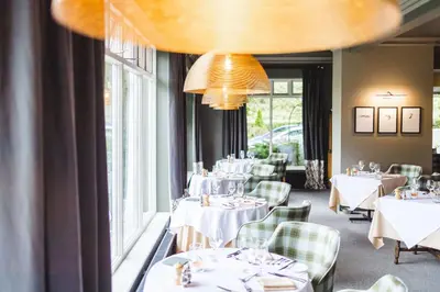 a restaurant with white tables and chairs and windows at Borrowdale Gates Hotel in Keswick